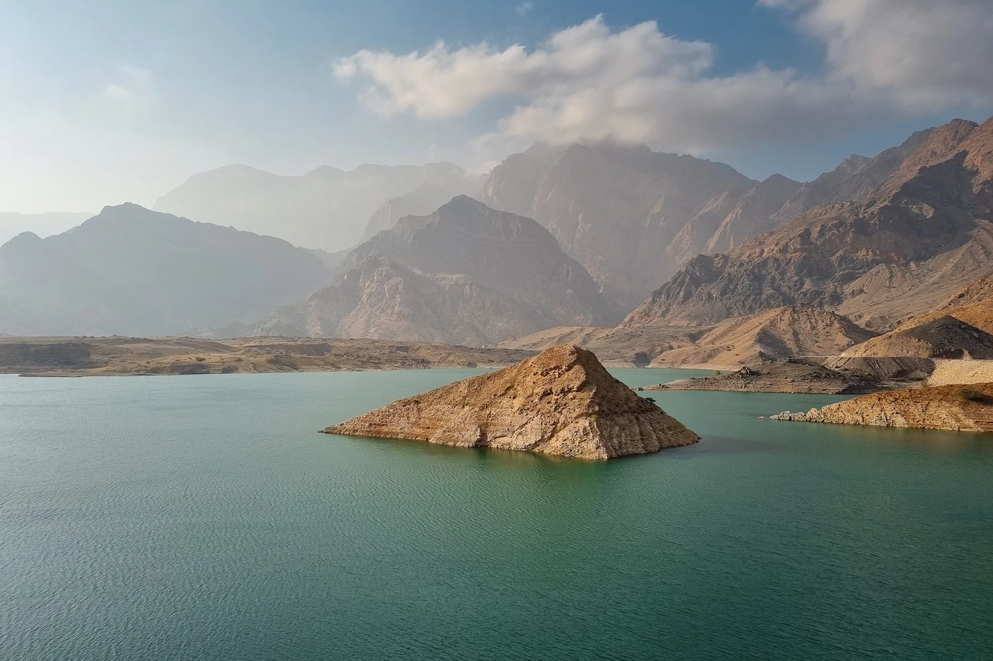 Rocky triangular peak emerging from the blue-green waters of Wadi Dayqah Dam, Oman.