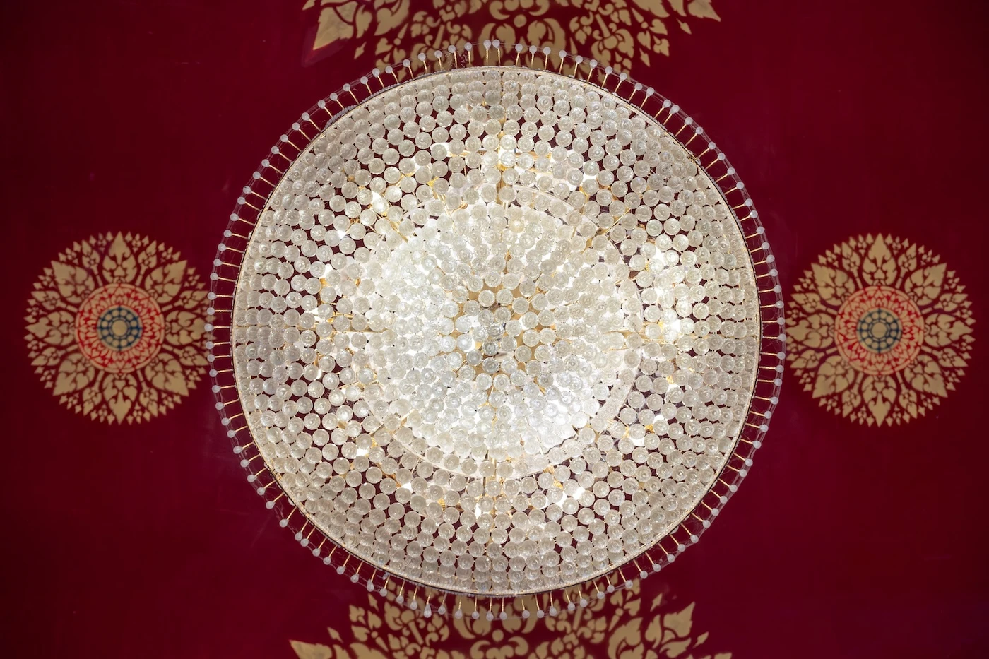 Ornate chandelier seen from below with red and gold roof above at Wat Bang Thong.