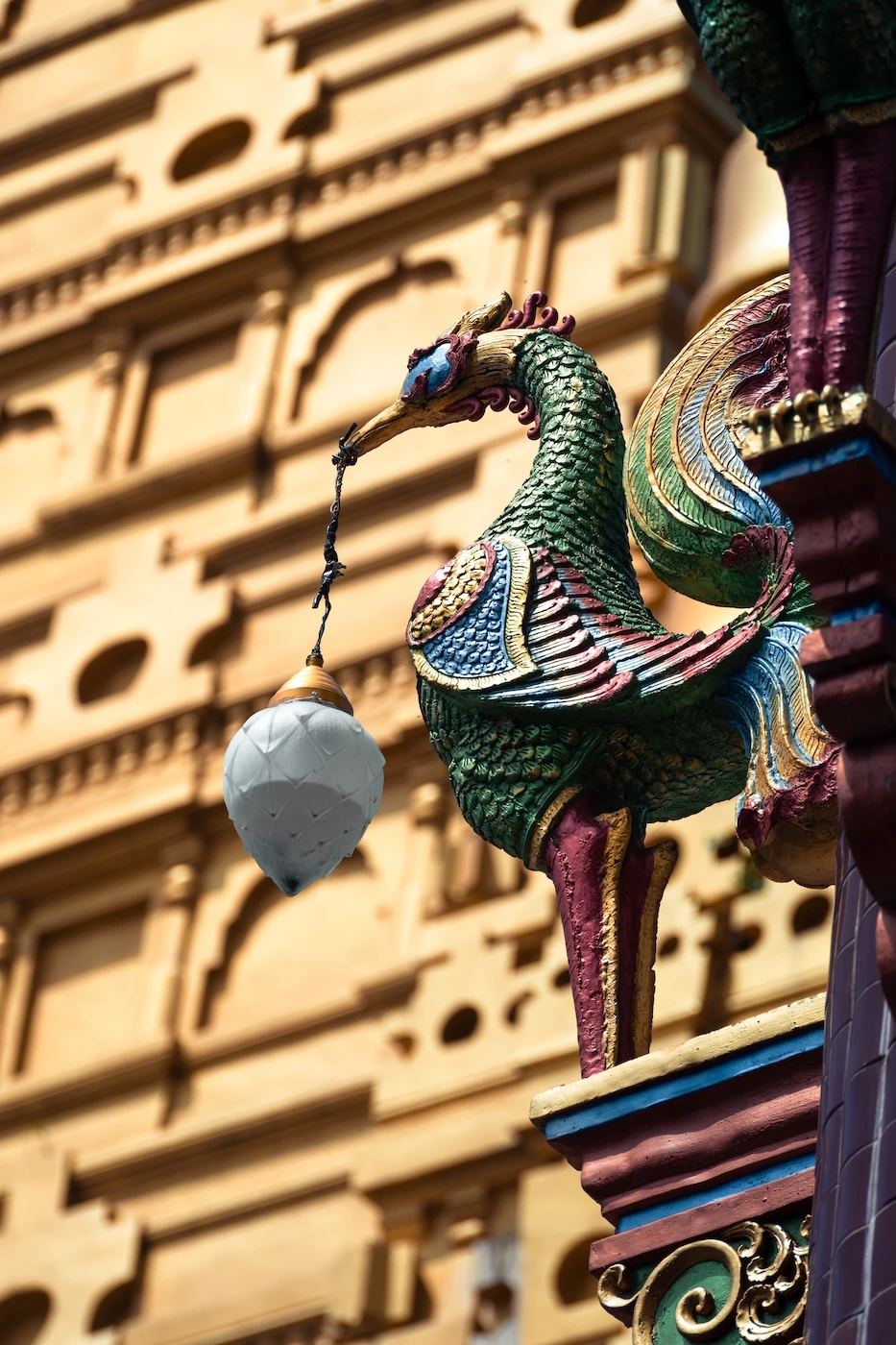 A colourful metal bird statue holding a lantern, sat atop a column at the Wat Bang Thong temple complex in Krabi.