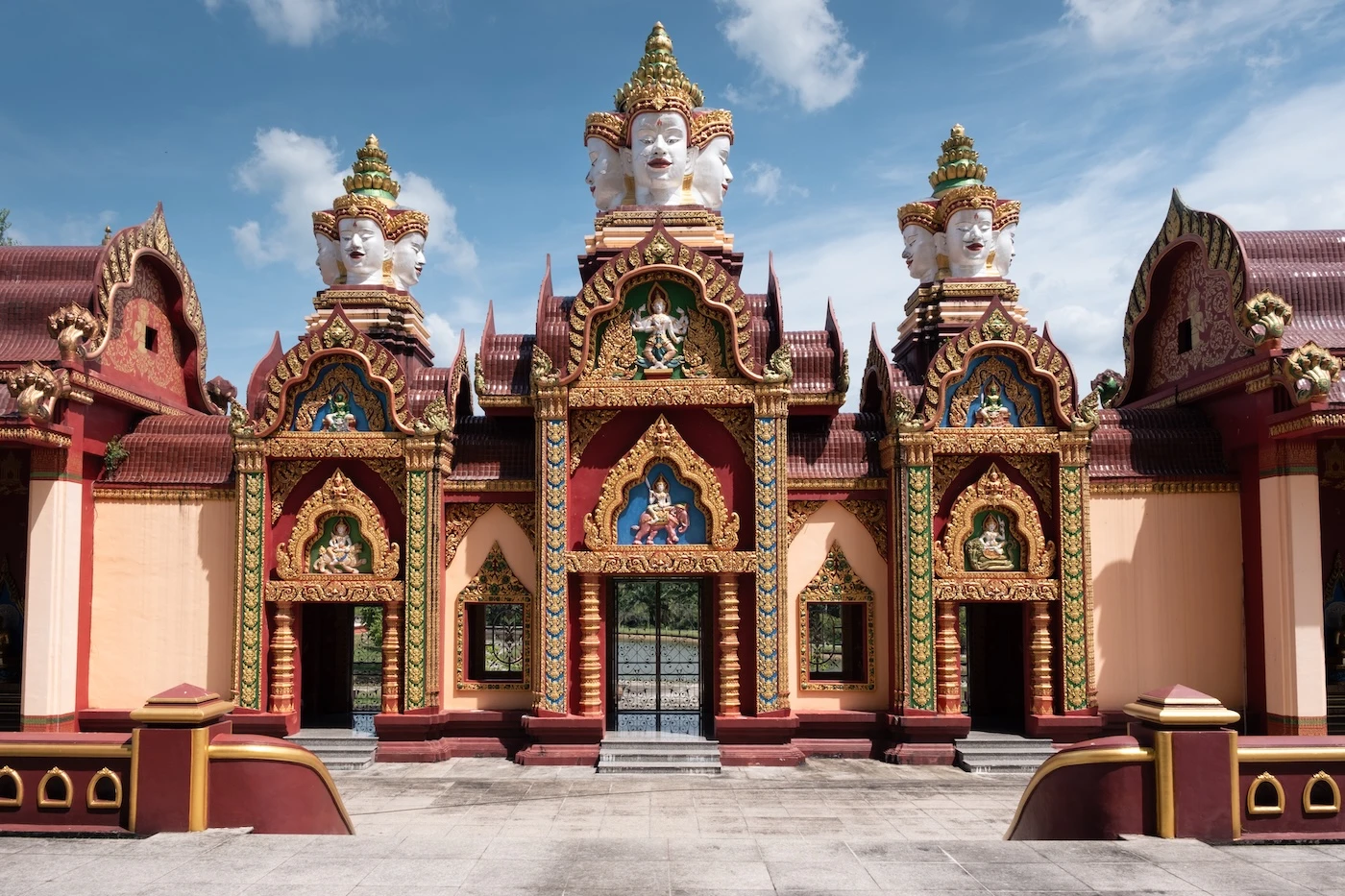 A set of three Four Headed Buddha statues atop entrances to a temple building.
