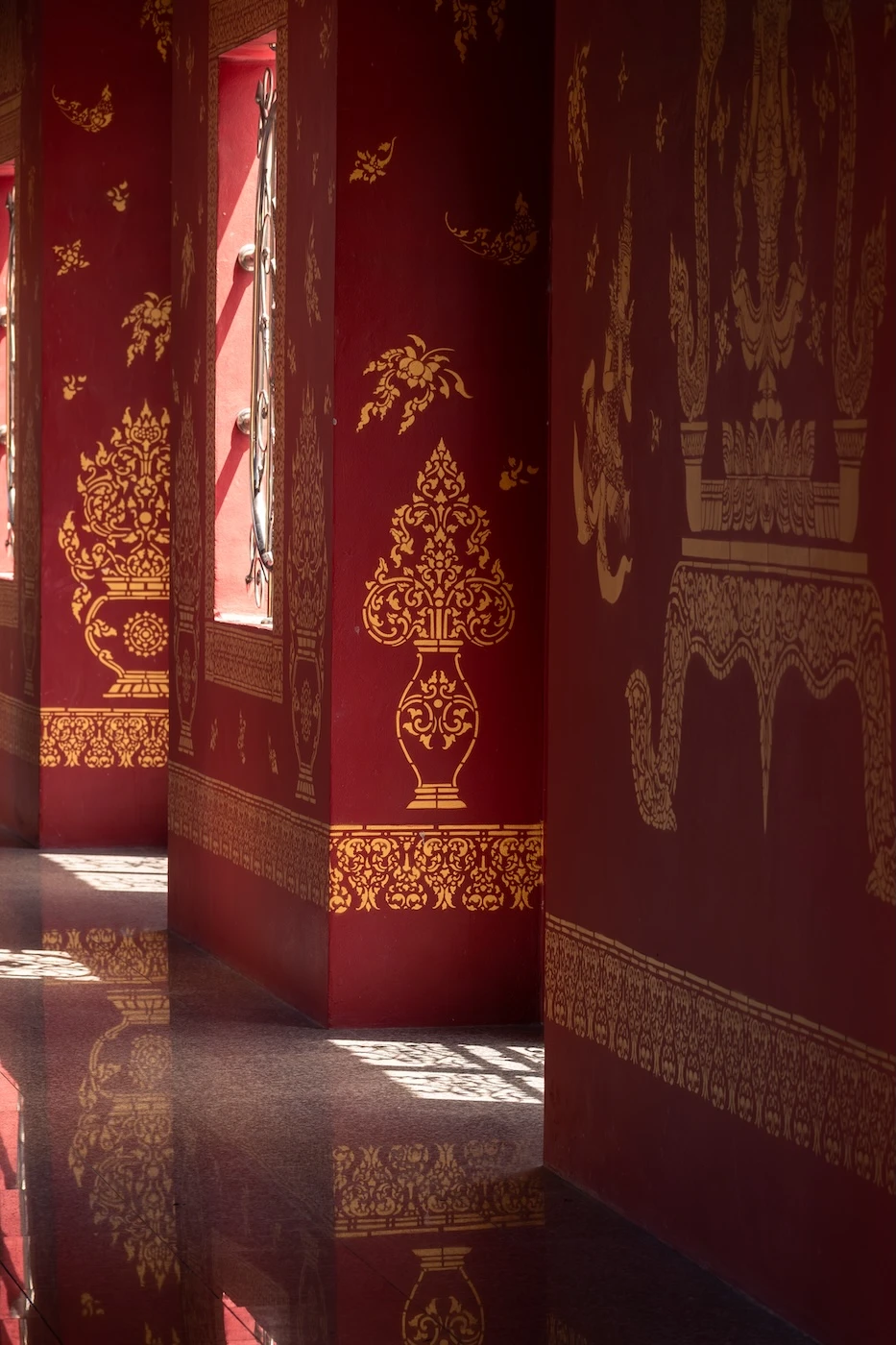 Red and gold temple decorations reflecting in the polished marble floor of Wat Bang Thong temple in Krabi.